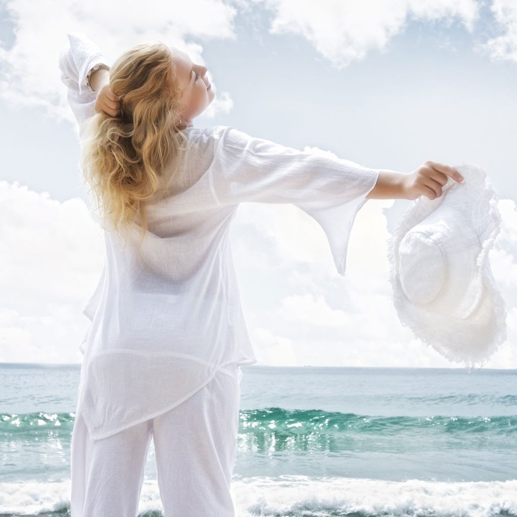 energised healthy woman at the beach looking carefree, wearing a white cotton loose fitting long top and trousers