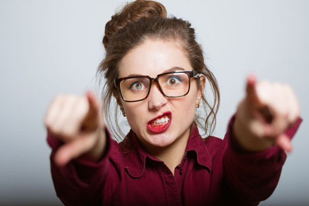 Women with hair in a bun, wearing a burgendy shirt blouse, in glasses and both arms stretched out in fornt of her while showing a grrr - I've got this - look on her face.