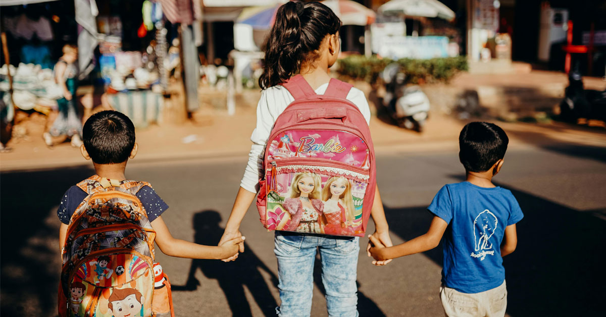 children walking to school with their mum, all wearing backpacks