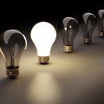 a single lit white light bulb along a row of unlit light bulbs with a darkish backlighting.