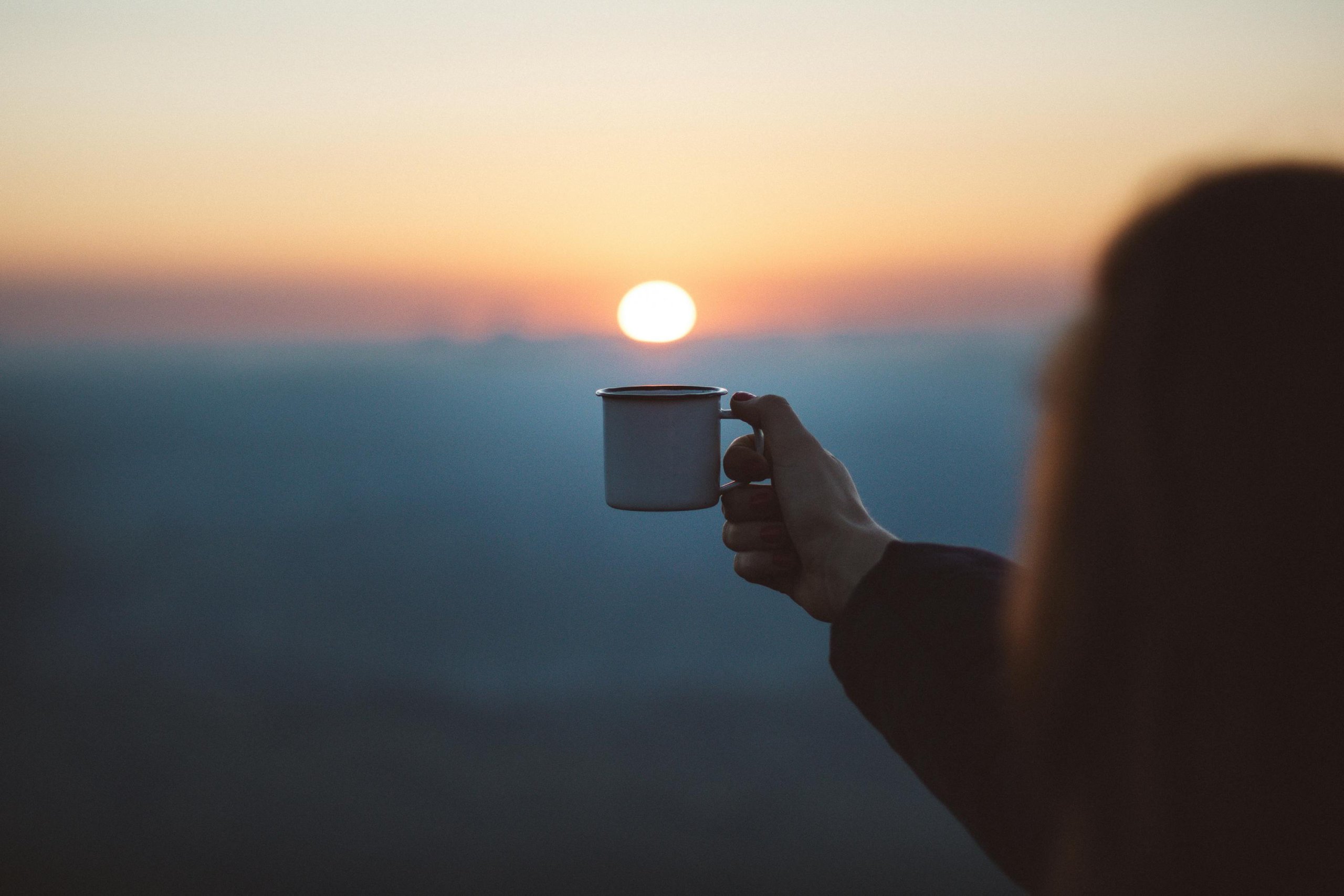 arm holding out a cup of hot tea when the sun is setting