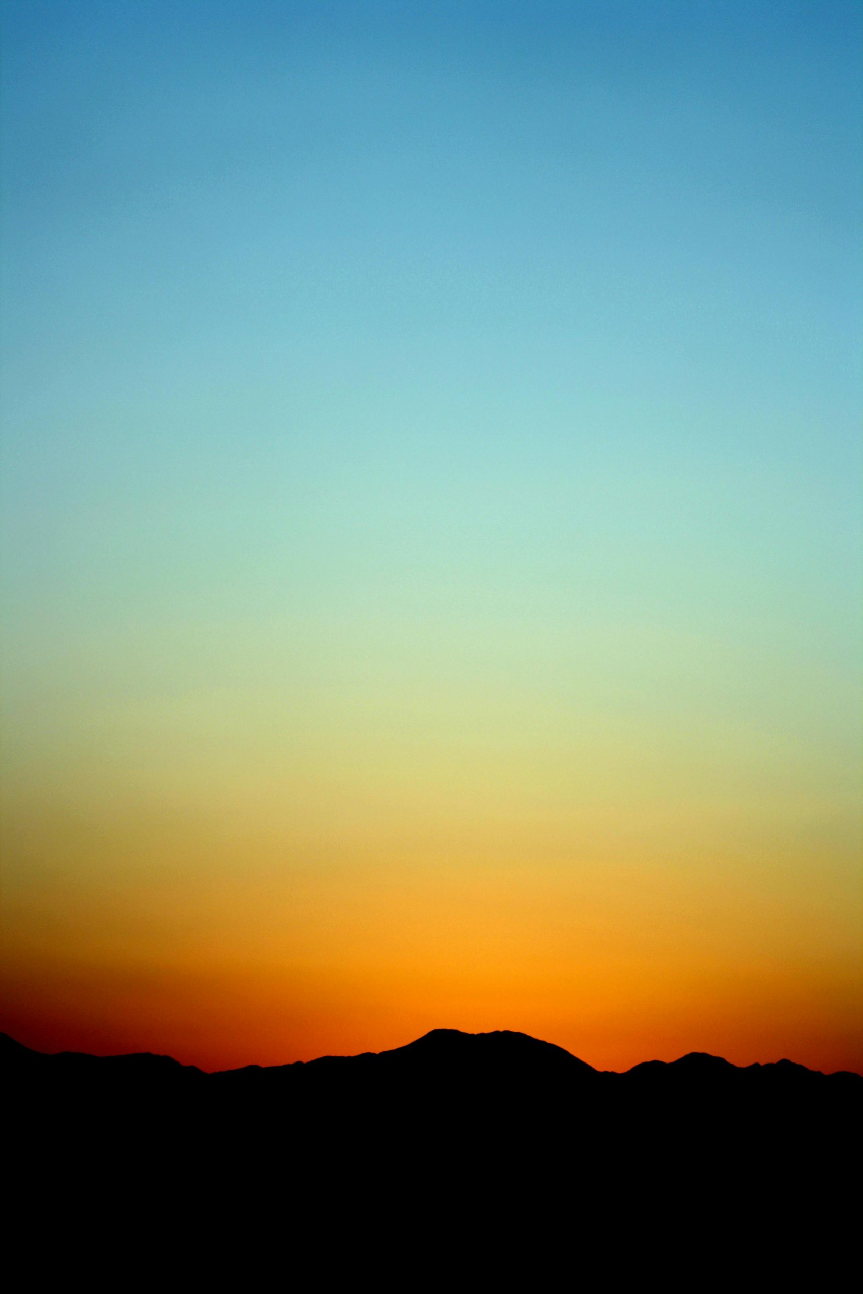 Sunset with turqoise sky with various hues of yellow and orange until you reach the dark outline of a hill and land.