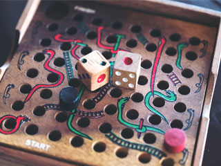 A vintage wooden game of snakes and ladders in dirty pink and turquoise green snakes and two dice sitting on top of the game