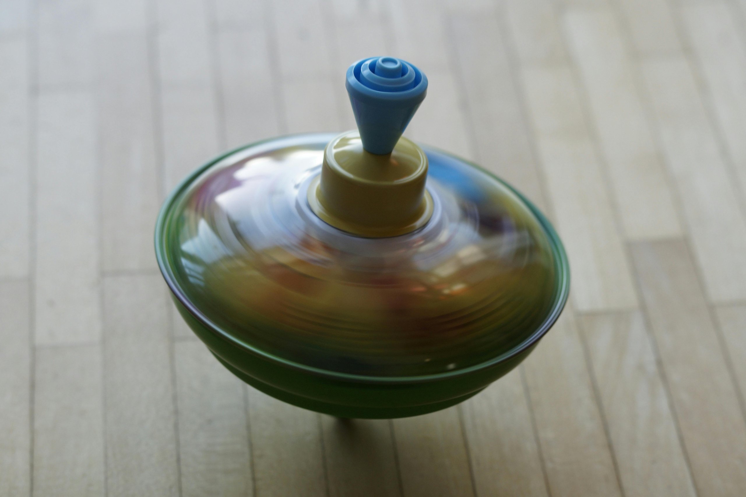 Spinning top in turquoise and bronze on a lightwood floor